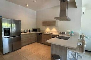 A modern kitchen with a central island, stainless steel appliances, and wooden cabinetry. - Waterfront Apartment in Marina (Rivière Noire District)