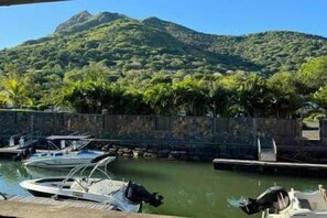 A marina with boats docked, a stone wall, and a mountain in the background. - Waterfront Apartment in Marina (Rivière Noire District)