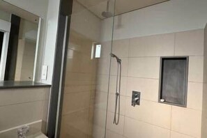A modern bathroom with a glass shower enclosure, a wall-mounted towel rack, and a small mirror. - Waterfront Apartment in Marina (Rivière Noire District)