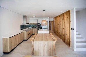 A modern kitchen with a central island, wooden paneling on the walls, and a dining area with a long table. - Luxury beachfront duplex and pool (Black River)