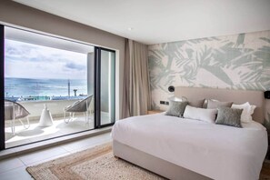 A bedroom with a large bed, a view of the ocean through a sliding door, and a balcony with chairs. - Luxury beachfront duplex and pool (Black River)