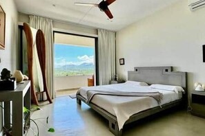 A hotel room with a bed, a desk, a chair, a ceiling fan, and a view of the outdoors. - Penthouse with Panoramic Sea Views (Tamarin)