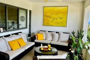 A living room with a sofa set, a coffee table with fruit, and a large yellow abstract painting on the wall. - Penthouse with Panoramic Sea Views (Tamarin)