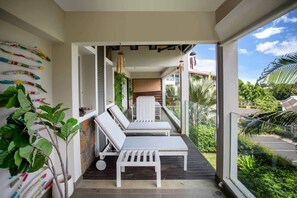 Ein Balkon mit zwei weißen Liegestühlen, einem Blumentopf und einer Wand mit bunten Objekten.