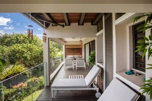 Un balcon avec un canapé blanc et un fauteuil de relaxation, donnant sur un jardin où poussent différentes plantes et sous un ciel dégagé.