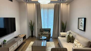 A modern living room with a flat-screen TV, a sofa, a coffee table, and a chandelier.