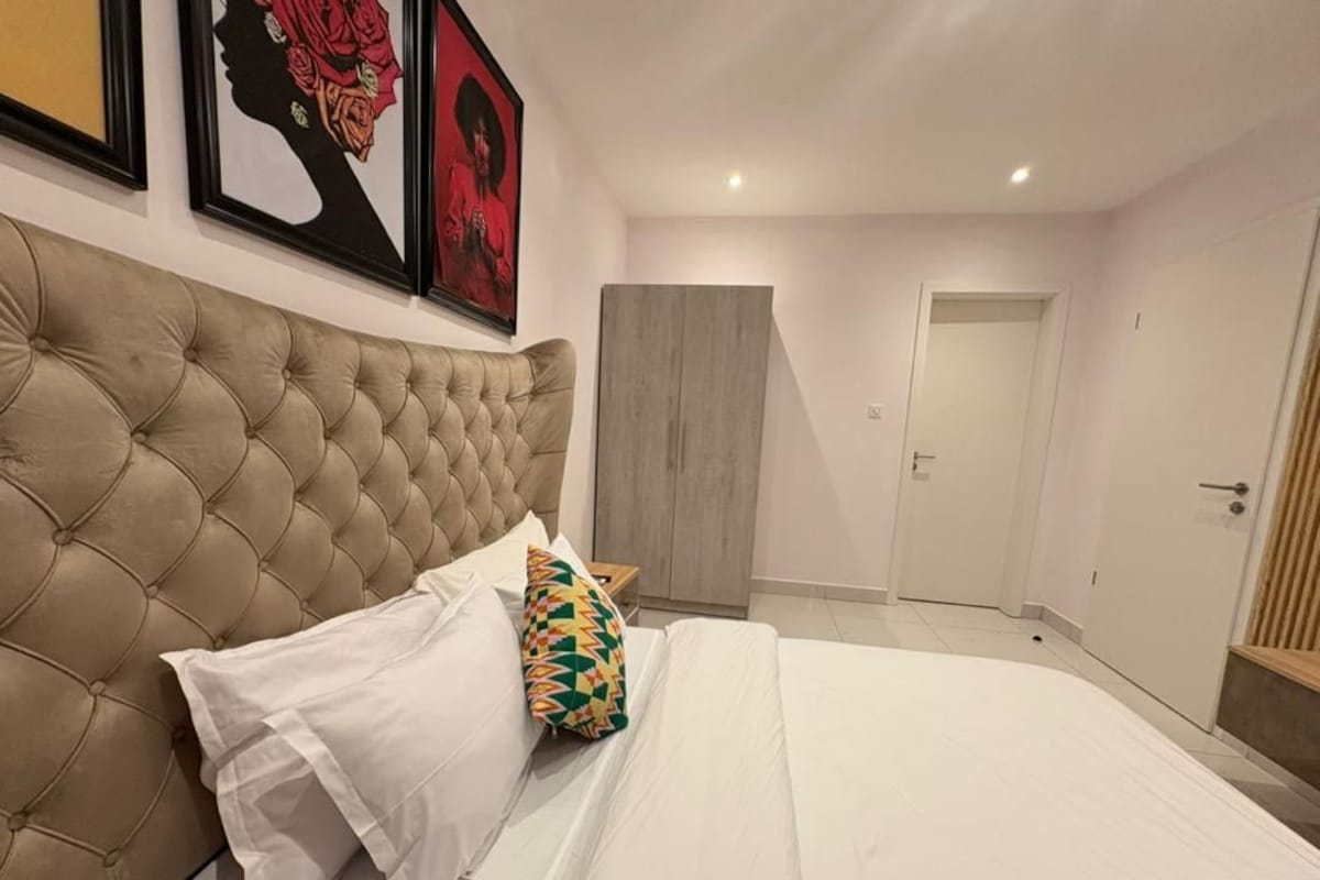 Quarto com cabeceira estofada, cama com roupa de cama branca, almofada colorida e guarda-roupa.
