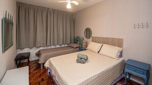Une chambre avec deux lits, un ventilateur de plafond, une table de chevet, un miroir et un porte-manteau.