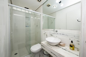Un baño moderno con ducha de vidrio, inodoro blanco y lavamanos de mármol con espejo arriba.