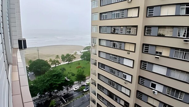 Un immeuble de grande hauteur doté de nombreux balcons, donnant sur une plage et une zone verdoyante.