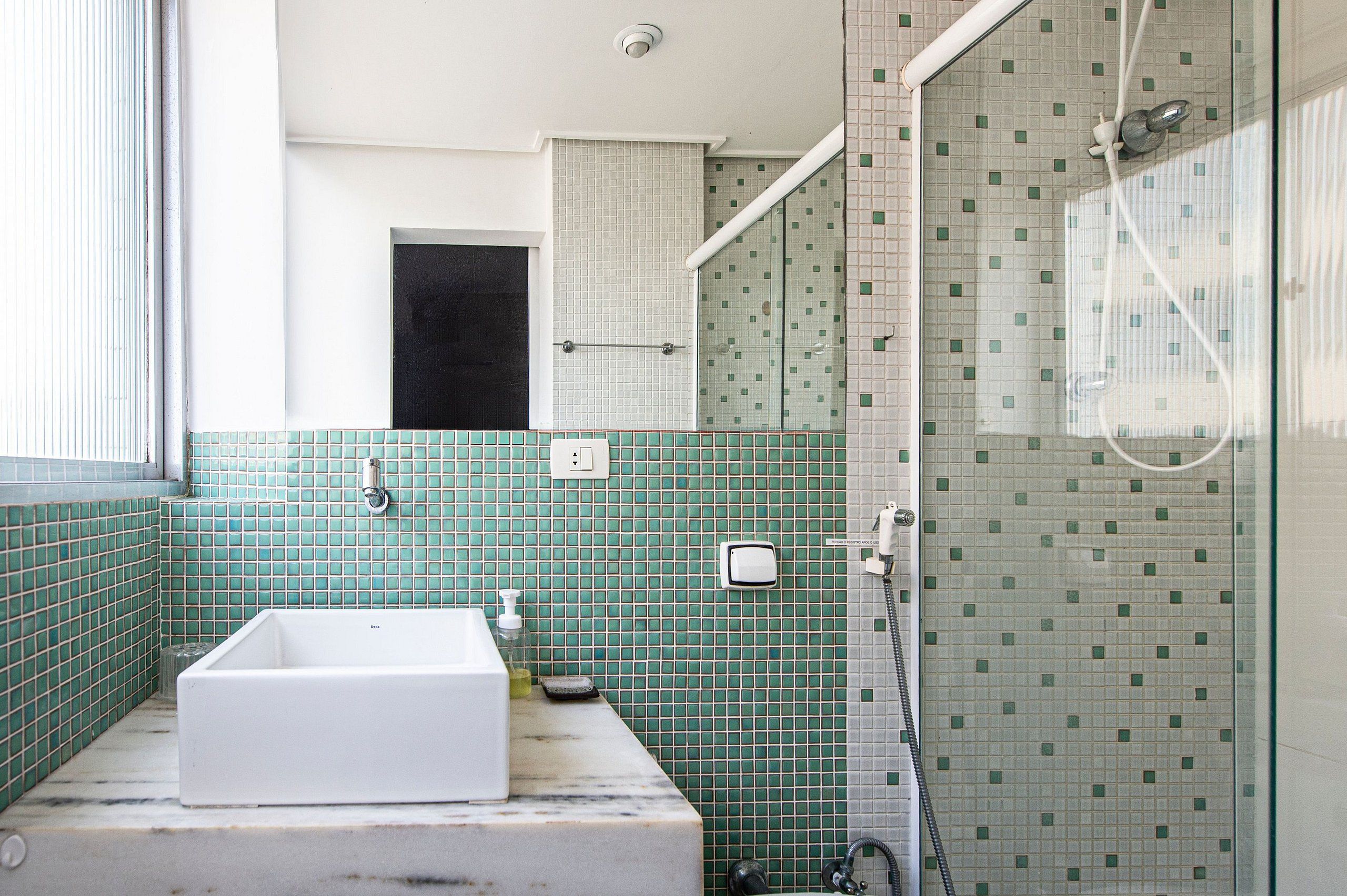 Un baño con bañera blanca, paredes cubiertas de azulejos verdes y una cabina de ducha de vidrio, además de una puerta visible.