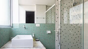 Un baño con bañera blanca, paredes cubiertas de azulejos verdes y una cabina de ducha de vidrio, además de una puerta visible.