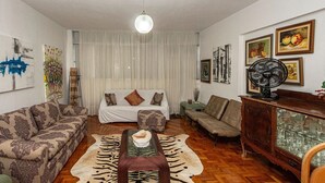 Un salon comprenant un canapé, un pouf et une table basse. On y trouve également un ventilateur et un meuble avec des portes en verre.