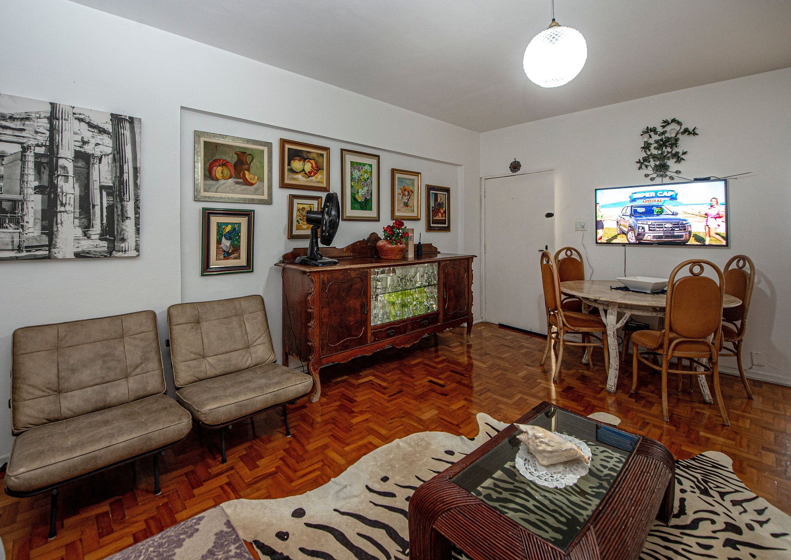 Una sala de estar con un conjunto de sofás, una mesa de comedor con sillas, un televisor montado en la pared y diversas obras de arte enmarcadas.