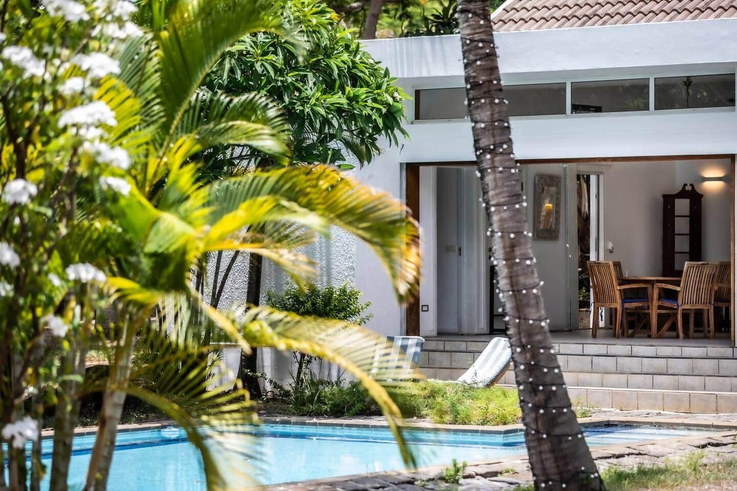 A poolside area with a clear view of a two-story building, outdoor furniture, and lush greenery.