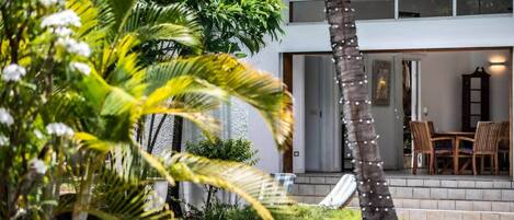 A poolside area with a clear view of a two-story building, outdoor furniture, and lush greenery.