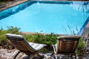 Two wooden lounge chairs with cushions facing a swimming pool.