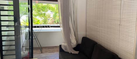 A room with a sliding glass door leading to a balcony, a dark-colored sofa, and a window with blinds.