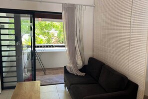 Ein Zimmer mit einer Schiebetür und Glasabschluss zum Balkon, einem dunkelbraunen Sofa und einem Fenster mit Jalousien.