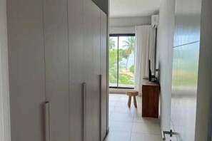 A corridor with a sliding door, a small stool, and a view of a balcony with a window. - Beachfront Luxury Villa & pool (Black River)