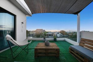 Terraço no telhado com vista para edifícios, uma cadeira branca, uma mesa de madeira e um banco.