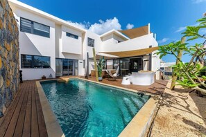 Ein modernes Haus mit Swimmingpool, Gartenmöbeln und einer Terrassenfläche.