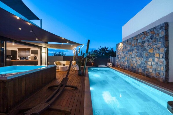 Ein moderner Poolbereich im Freien mit Whirlpool, Holzterrasse und Steinwand.