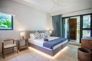 A modern bedroom with a bed, bedside tables, a chair, and a view of the outdoors. - Beachfront Villa with Private Pool (Black River)