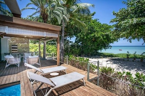 A wooden deck with lounge chairs and a pool, overlooking a beach and ocean.