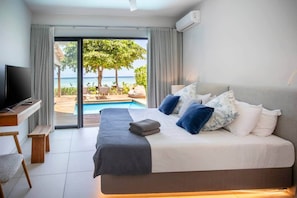 A hotel room with a bed, a TV, a desk, and a view of the ocean.