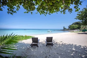 A beach with two sun loungers facing the ocean, clear skies, and a calm sea.
