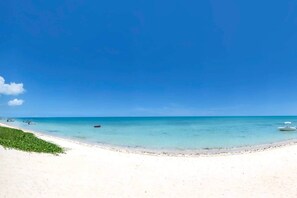 A beach with clear turquoise water, a sandy shore, and a few boats. - Beachfront Villa with Private Pool (Black River)