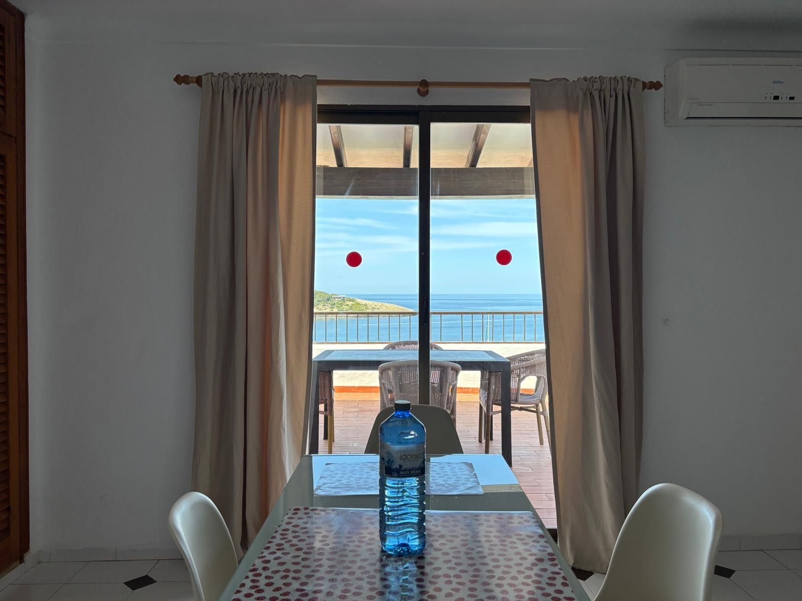 A room with a table and chairs, a bottle of water, and a view of the sea through a glass door.