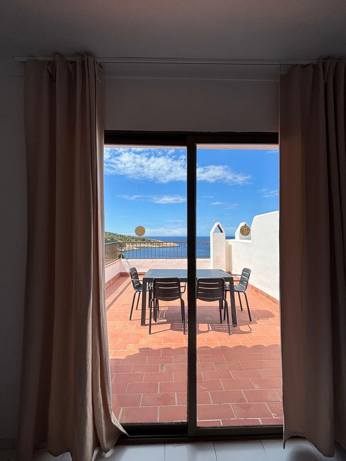 Un balcón con mesa y sillas, con vistas a la costa y un cielo despejado.