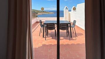 Un balcón con mesa y sillas, con vistas a la costa y un cielo despejado.
