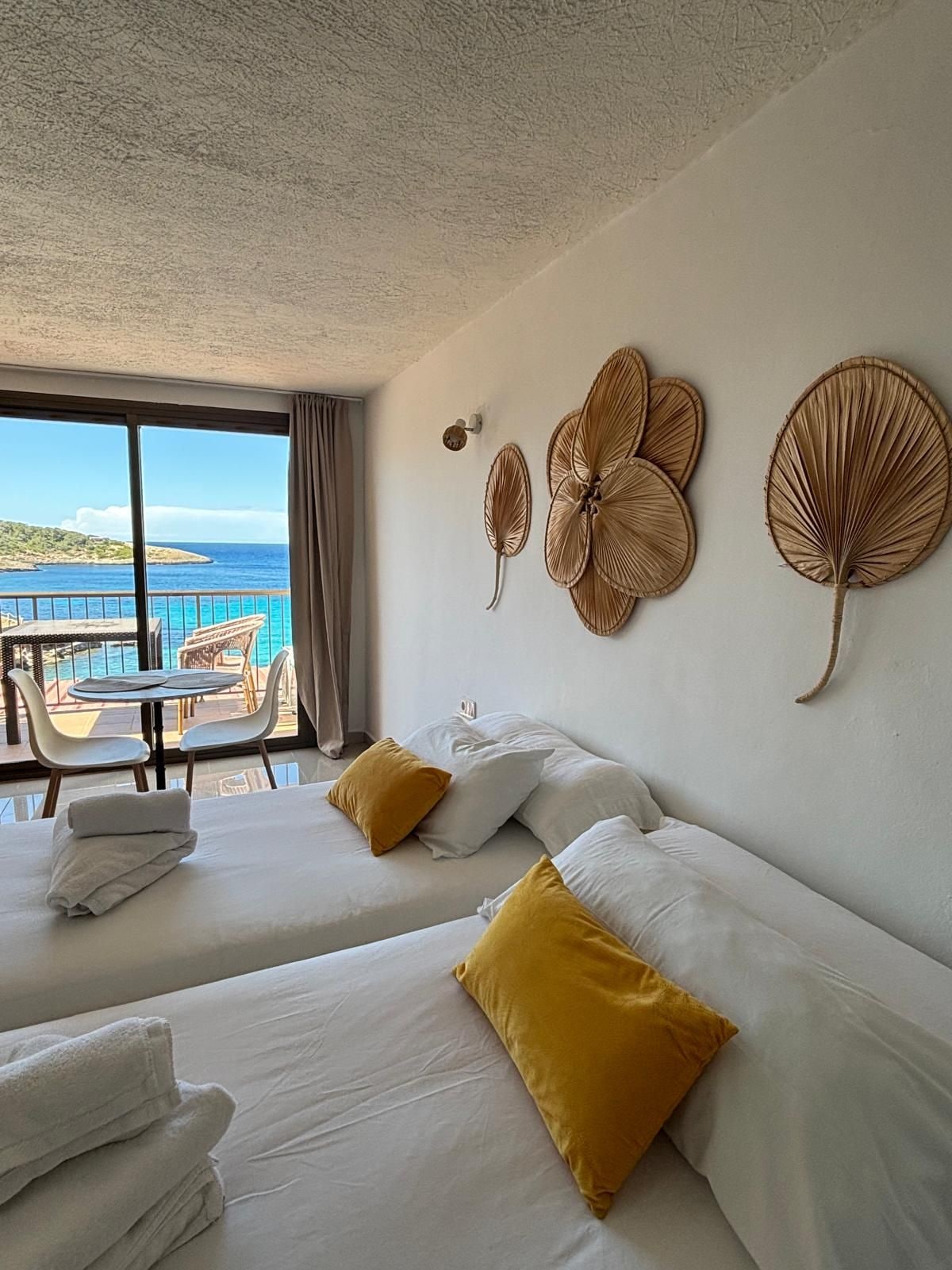 Een hotelkamer met twee bedden, een balkon met uitzicht op zee en decoratieve wandkunst.