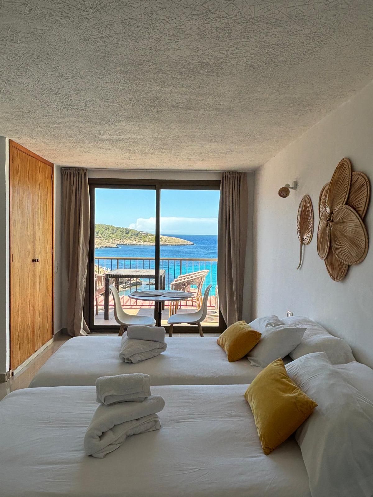 Een hotelkamer met een bed, een tafel met stoelen, uitzicht op zee en een balkon.
