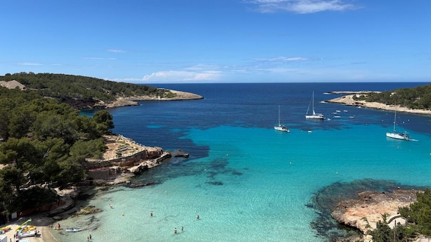 A coastal area with clear turquoise waters, boats, and a rocky shoreline. - es grop apartamentos (Portinatx)