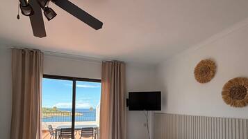 A hotel room with two beds, a ceiling fan, a TV, and a balcony with a view of the sea.