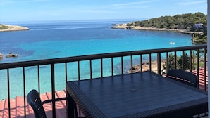 A balcony with a table and chairs overlooking a coastal view. - es grop apartamentos (Portinatx)