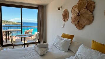 Une chambre d’hôtel avec balcon, un lit avec du linge de maison blanc et une vue sur la mer.