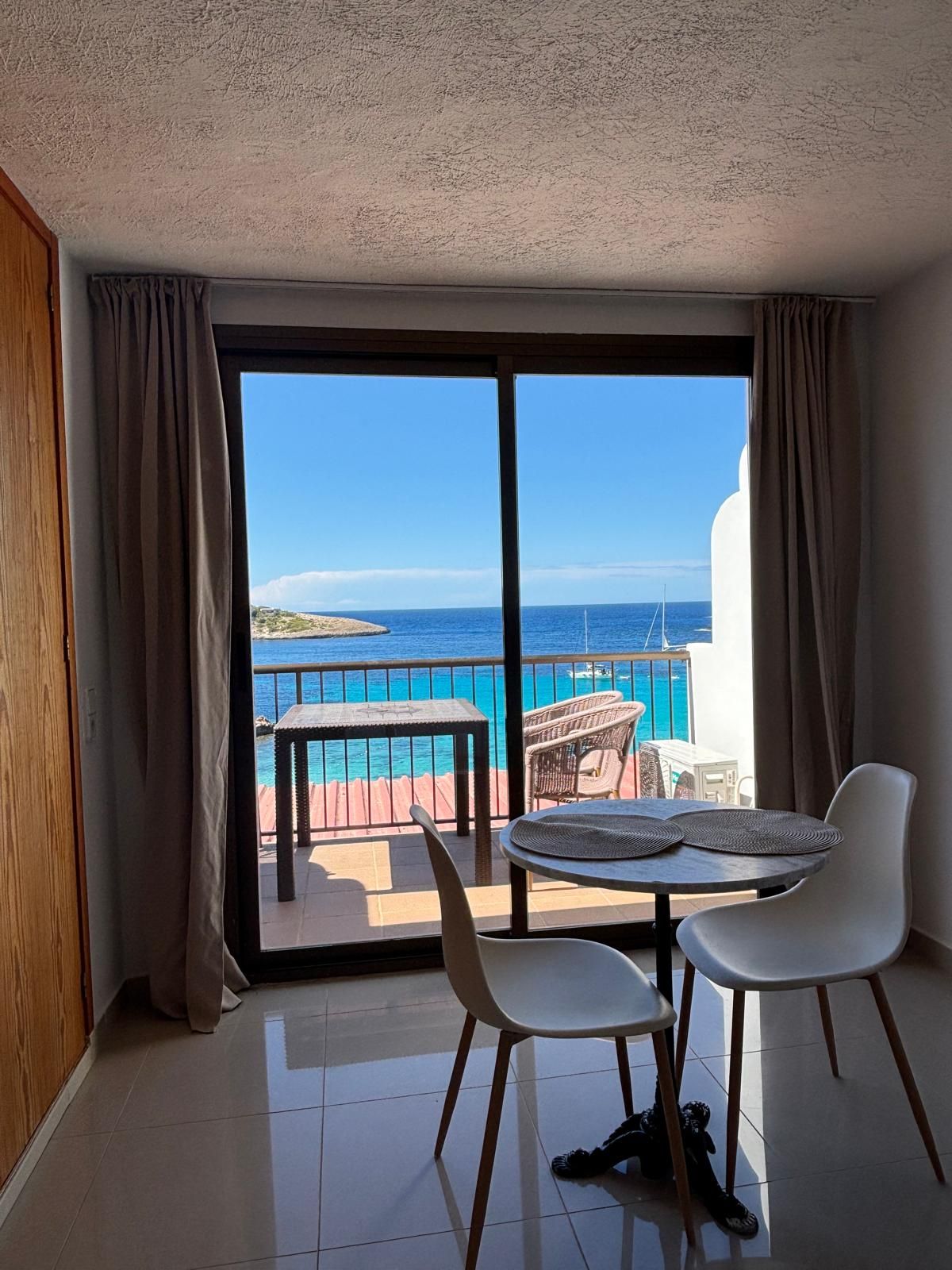 Ein Zimmer mit Meerblick, ein Balkon mit Tisch und Stühlen und zwei weiße Stühle im Inneren.