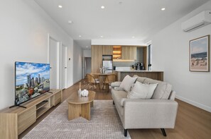 A modern living room with a sofa, coffee table, and a television displaying a cityscape. - Skydeck 2-bed Residence Near Albert Park (Melbourne)