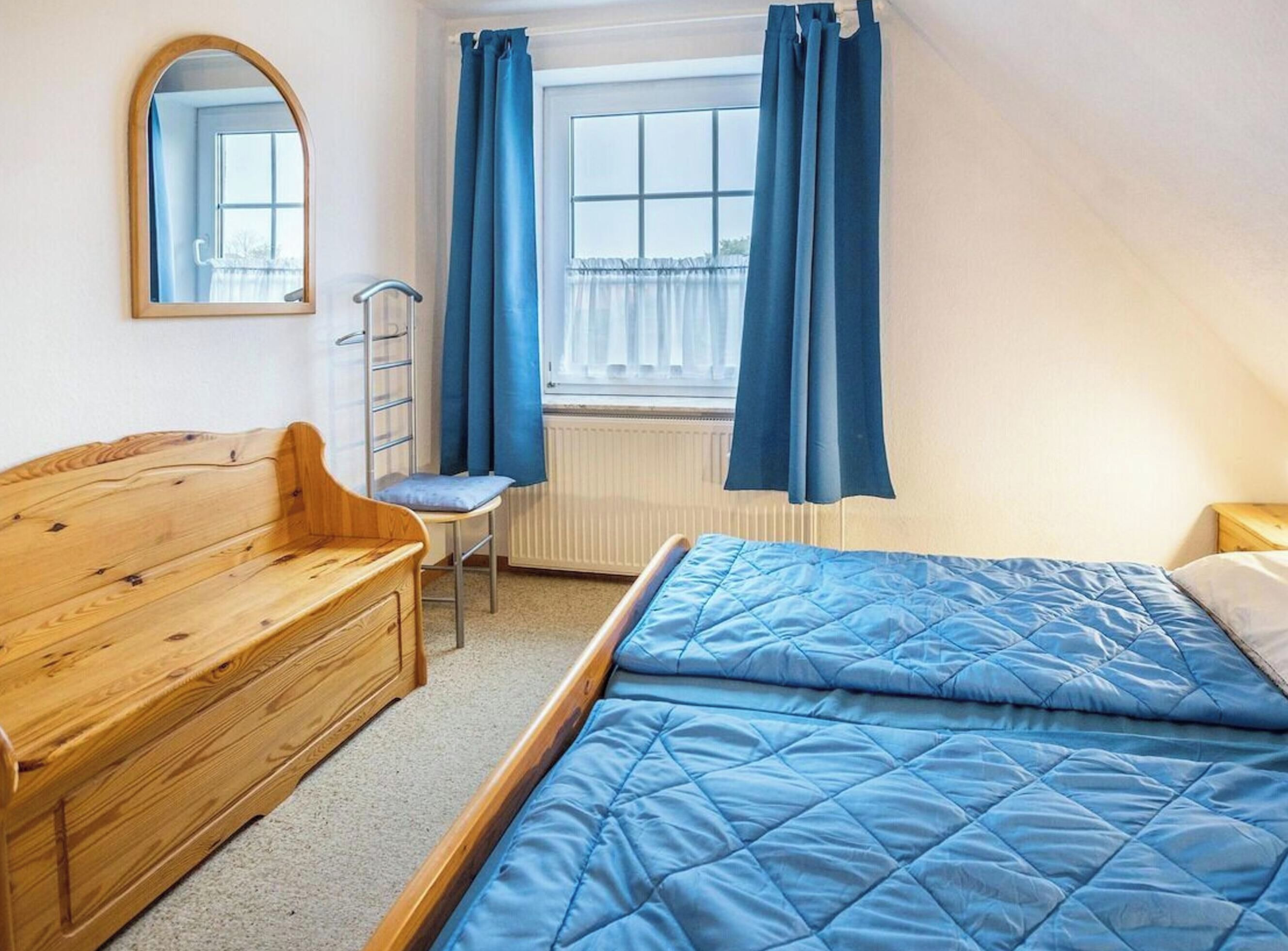 Een slaapkamer met een houten bed, een stoel, een klein tafeltje, een radiator en een raam met gordijnen.