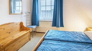 Een slaapkamer met een houten bed, een stoel, een klein tafeltje, een radiator en een raam met gordijnen.