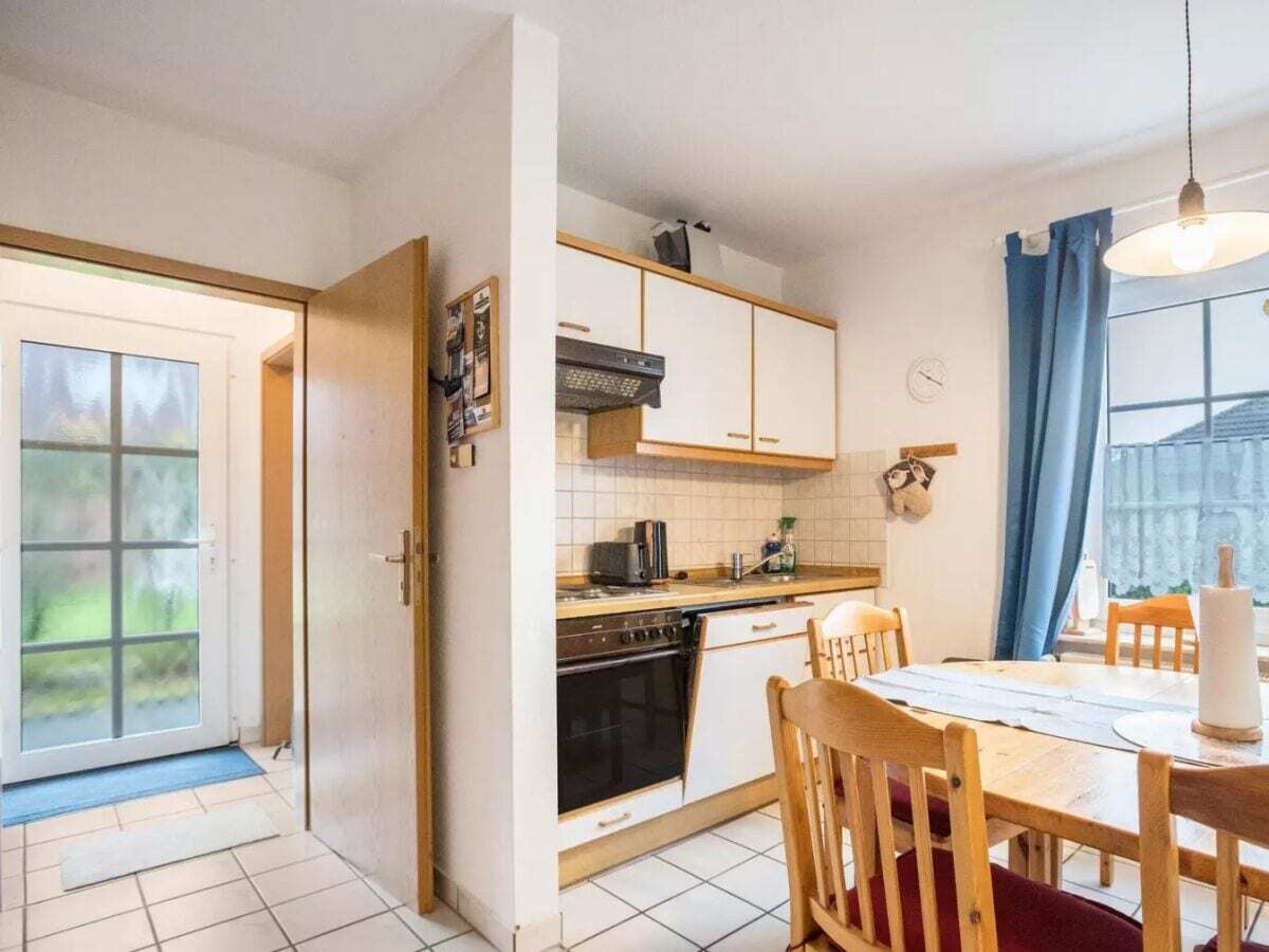 A kitchen with a dining area, a stove, oven, and a window with curtains.