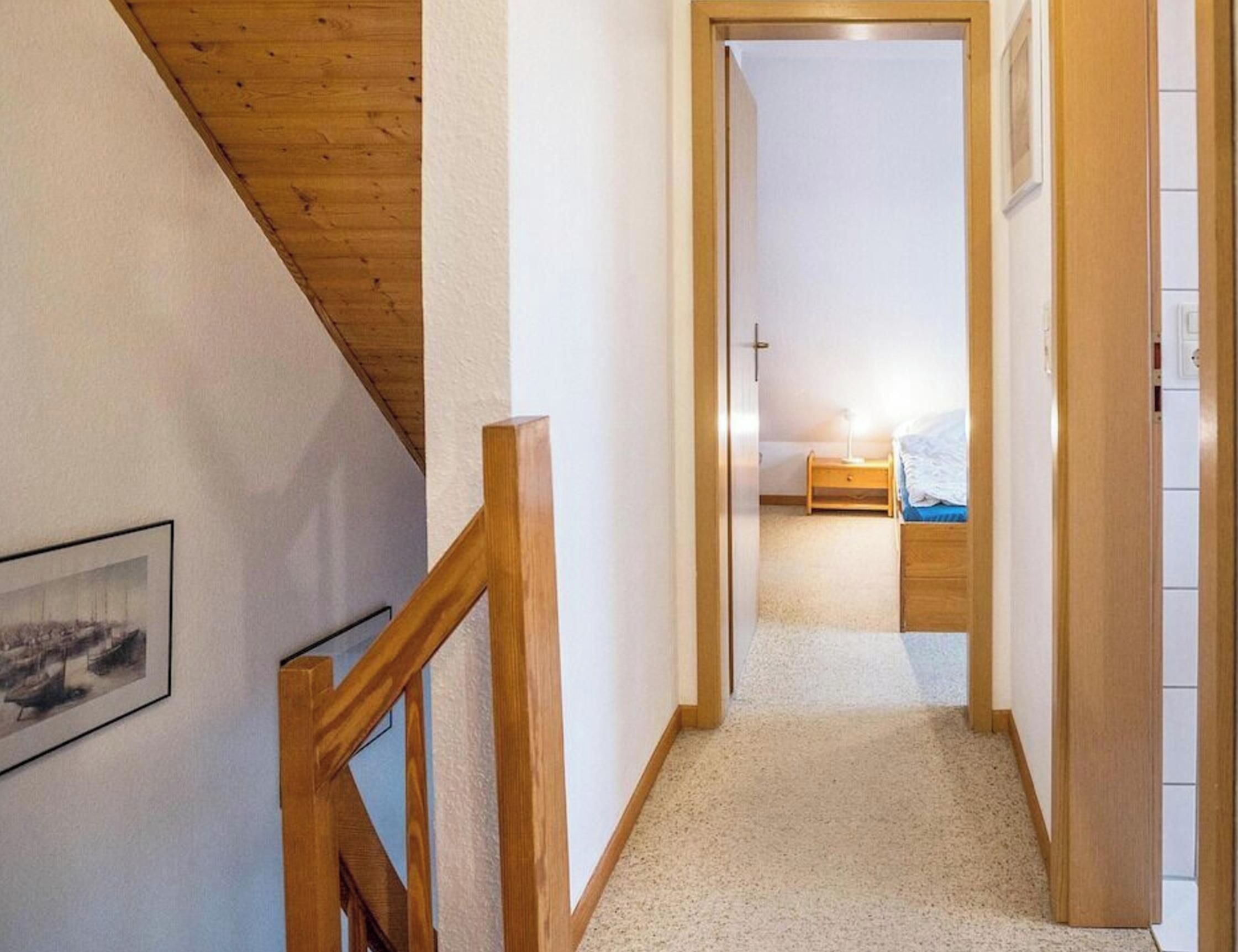 A narrow hallway leading to a bedroom with a bed and a nightstand.