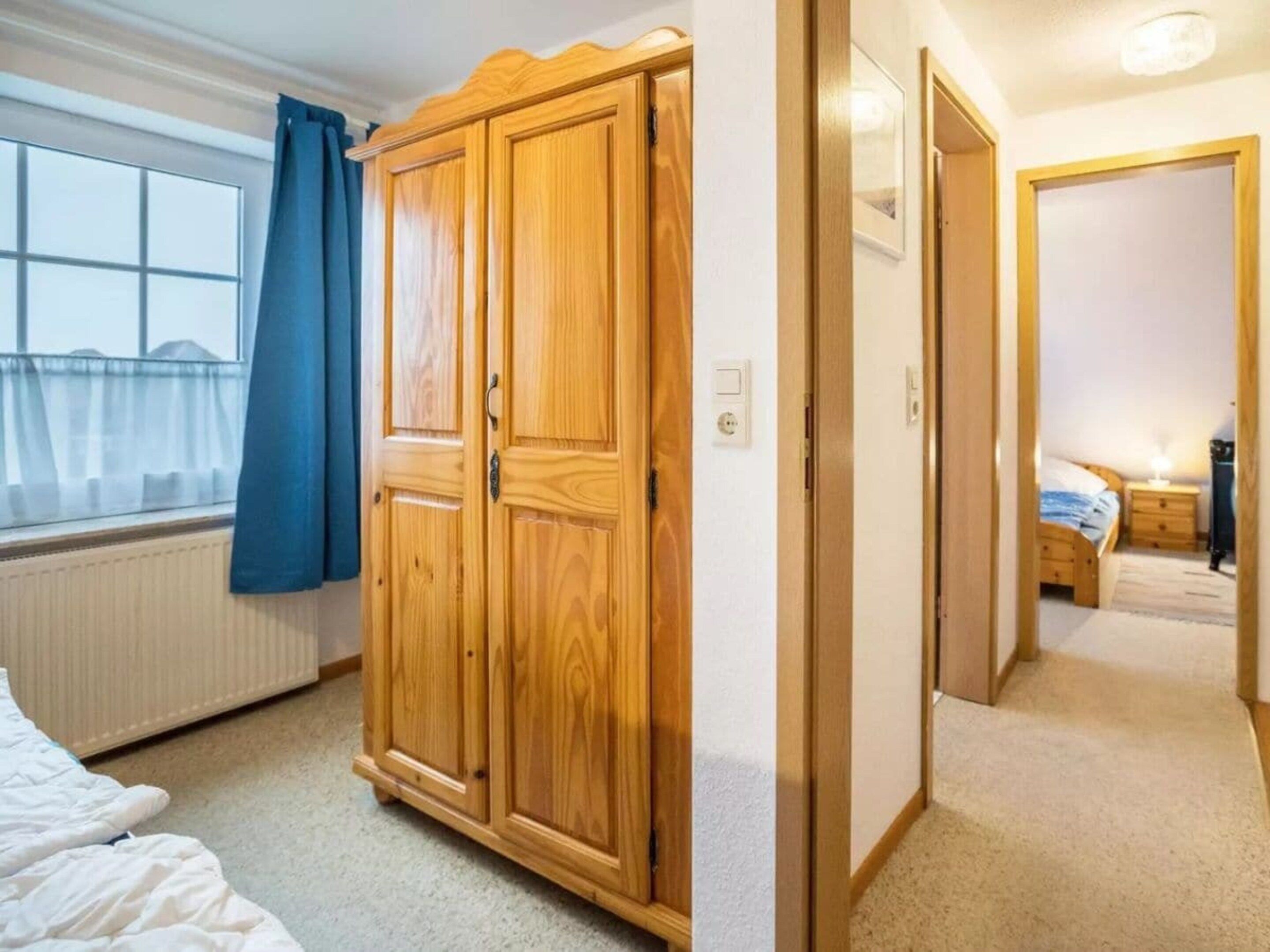 Ein Schlafzimmer mit großem Holzschrank, Fenster mit blauen Vorhängen und Blick auf die Stadt.