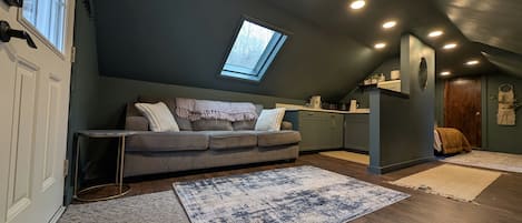 A loft-style living space with a sloped ceiling, a skylight, a sofa, a coffee table, and a kitchen area.