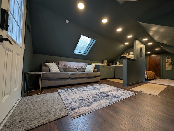 A loft-style living space with a sloped ceiling, a skylight, a sofa, a coffee table, and a kitchen area. - Cozy Loft Retreat- Walk to Liberty Mountain Resort (Fairfield)